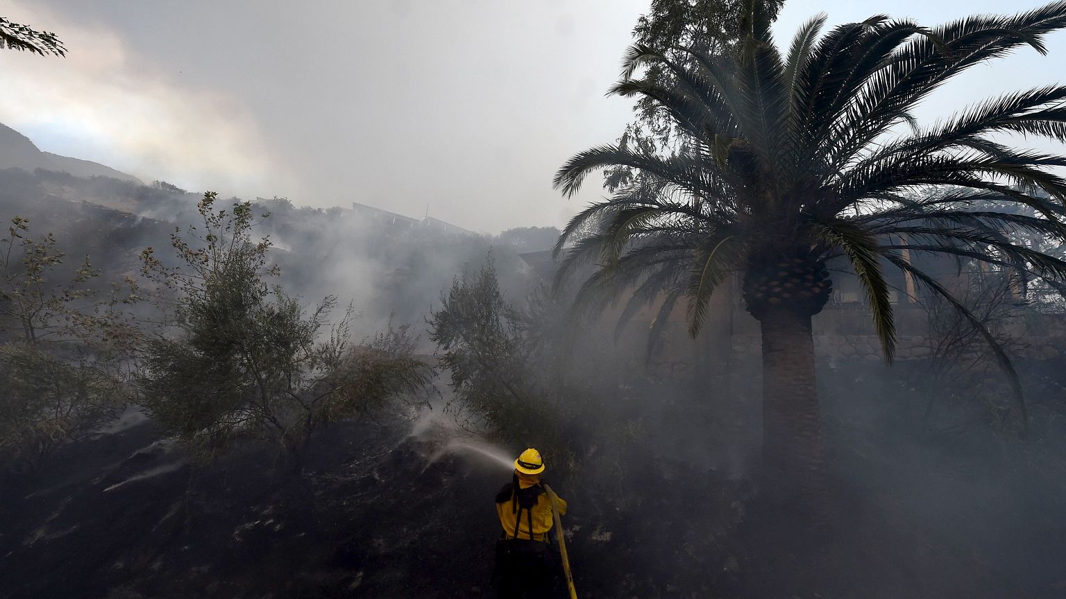 Image: A firefighter puts out hotspots on a smoldering hillside in Montecit