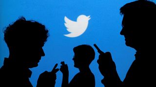 Image: People holds mobile phones in front of a Twitter logo in an illustra