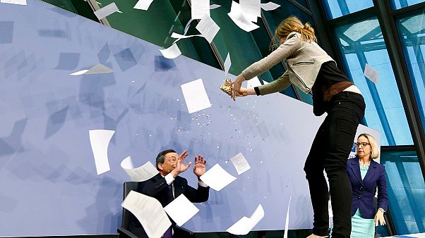 محتجة يهاجم رئيس المركزي الأوروبي خلال مؤتمر صحفي محتجة يهاجم رئيس المركزي الأوروبي خلال مؤتمر صحفي