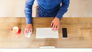 Image: A man uses a computer on a tidy desk