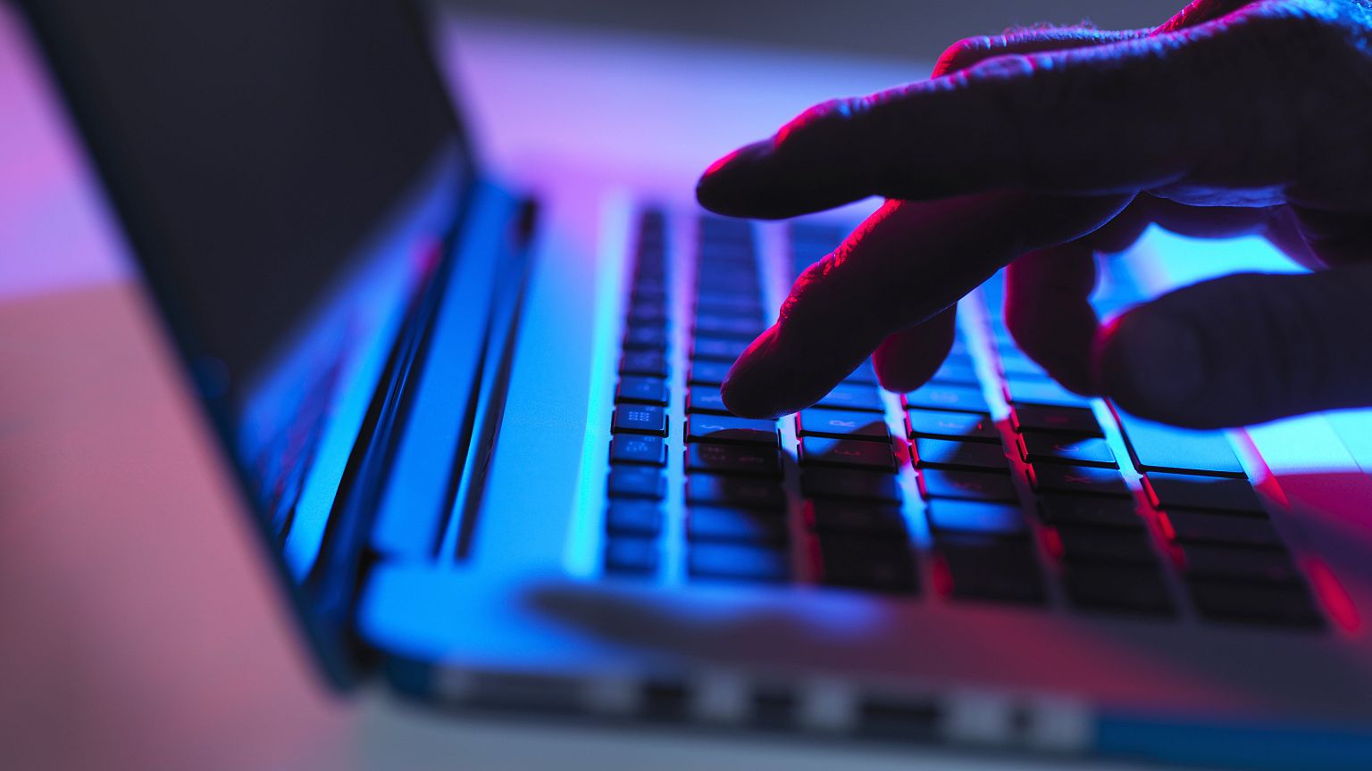 Image: Silhouette of male hand typing on laptop keyboard at night