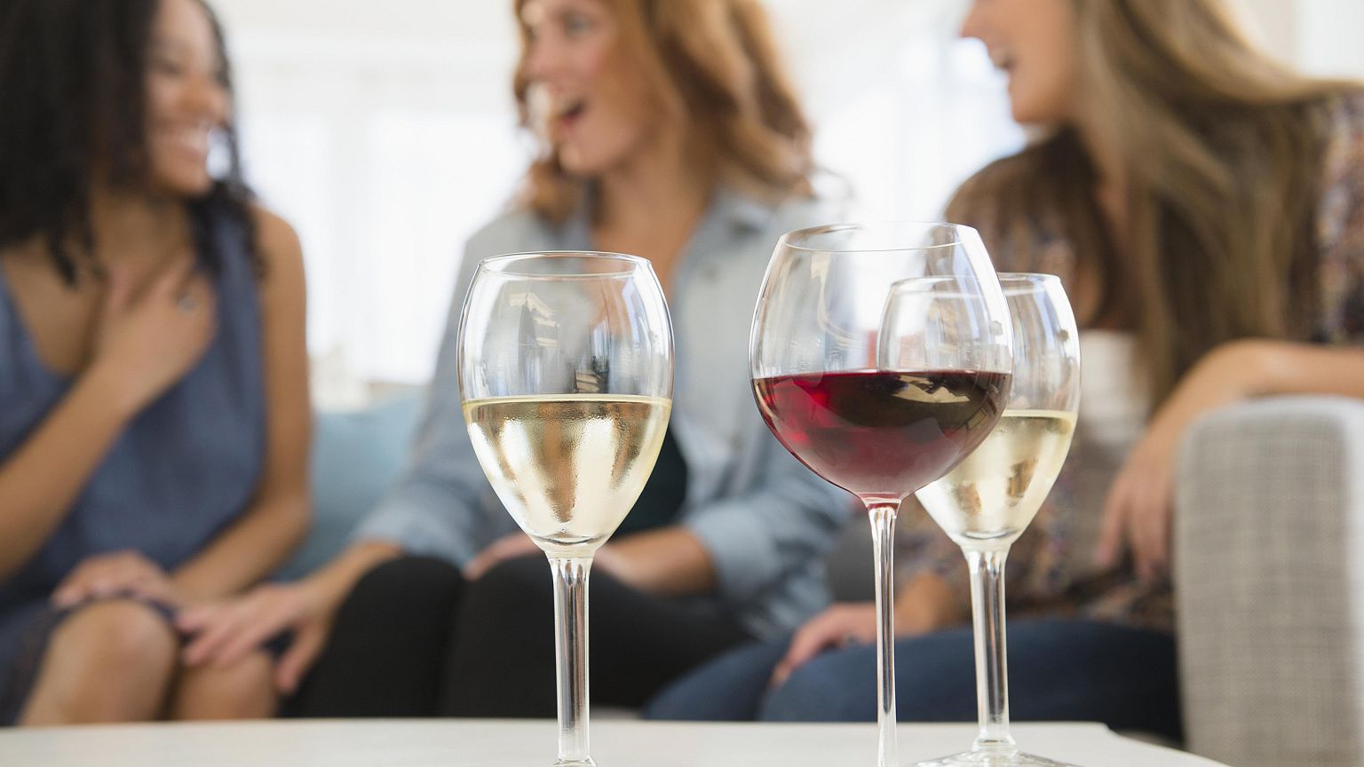 Image: Women drinking wine and talking on sofa in living room