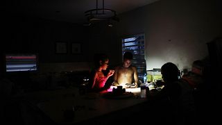 Image: Family members eat dinner at dusk with light from a cell phone