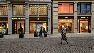 Image: People walk along a strip of designer storefronts in Oslo, Norway.