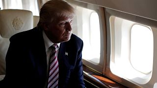 Image: Trump looks out the window as he travels aboard his plane between ca
