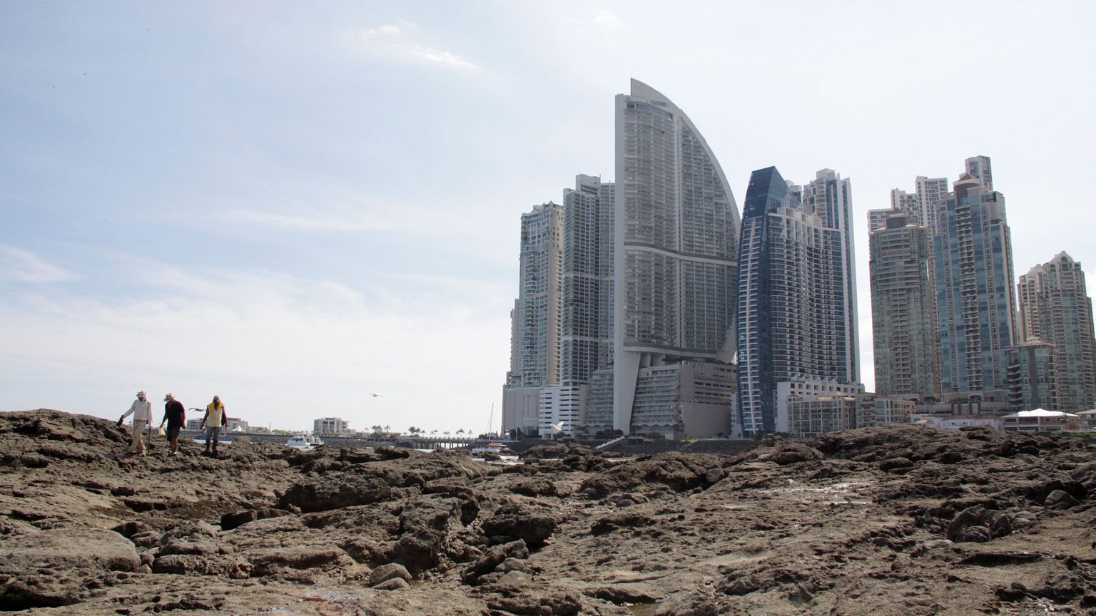Image: People stand on rocks on the shore during low tide as the Trump Ocea