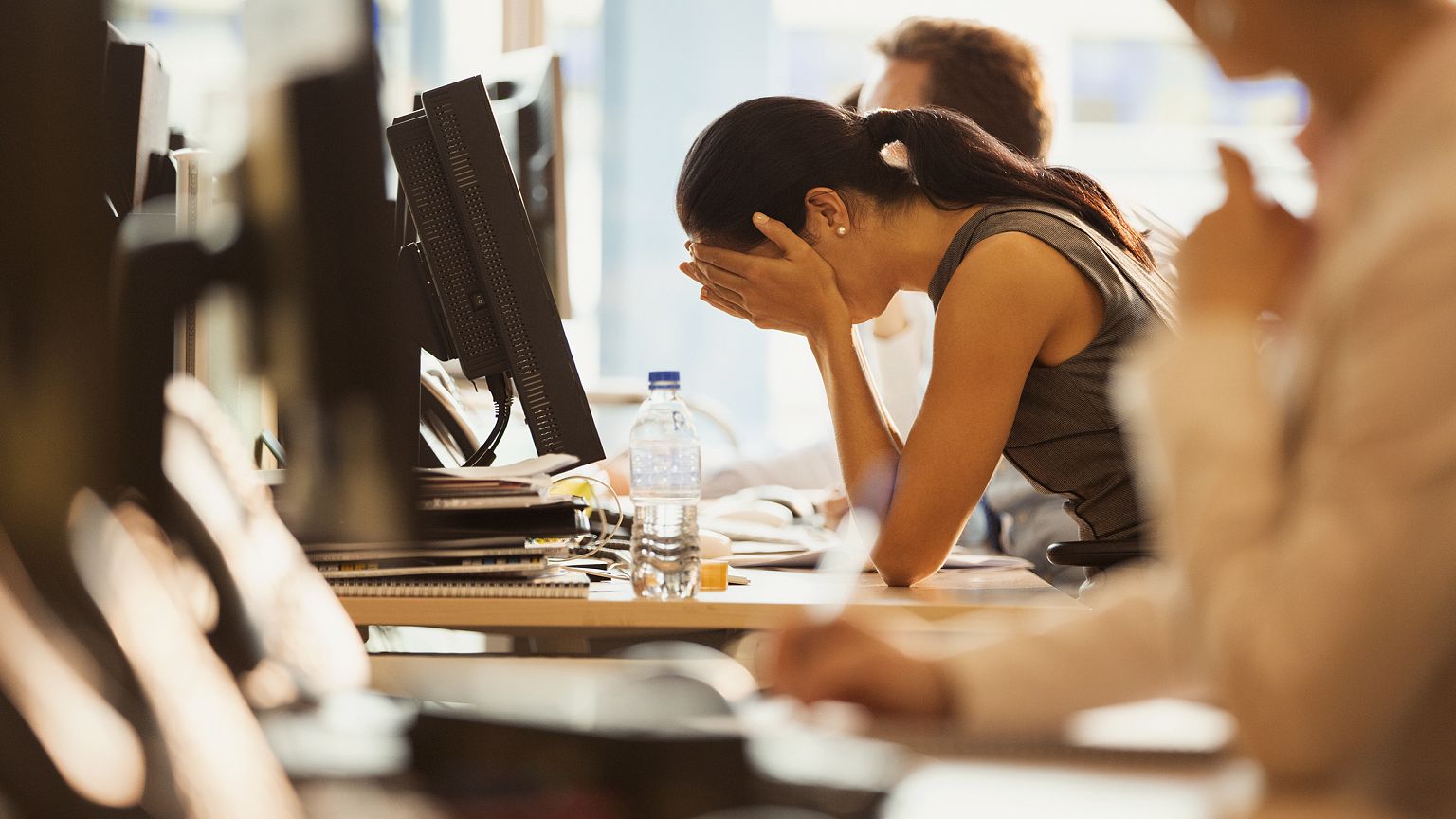 Image: Stressed woman sits with her head in her hands at an office desk