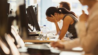 Image: Stressed woman sits with her head in her hands at an office desk