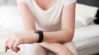 Cropped shot of a woman sitting on bed wearing a smart watch
