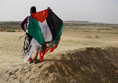 A Palestinian youth holds a kite with the colors of his national flag at the site of protest tents next to the Gaza Strip\'s border fence with Israel