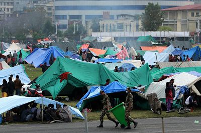 Nepalese military personnel carry rubbish bins as victims of an earthquake walk about outside their tents at a makeshift camp in Kathmandu, Nepal on April 28, 2015.