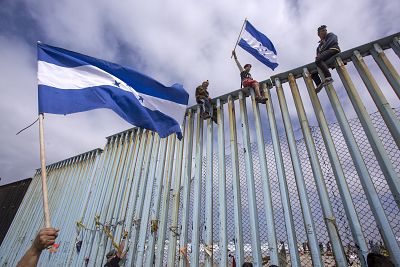 TIJUANA, MEXICO - APRIL 29: People hold Honduran flags at the border fence during a rally with members of a caravan of Central American asylum seekers and supporters on April 29, 2018 in Tijuana, Baja California Norte, Mexico.  (Photo by David McNew/Getty Images)