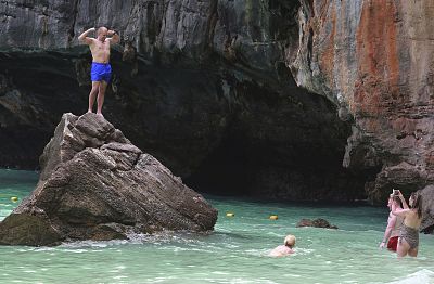 Tourists pose for photos on an outcropping in Maya Bay, Thailand.