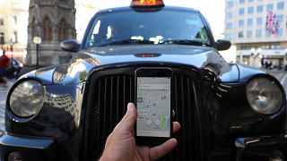 Image: A photo illustration shows the Uber app and a black cab in London,