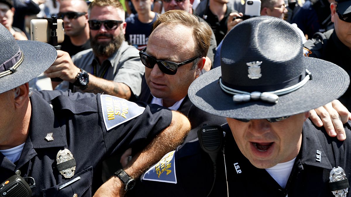 Image: Alex Jones, center, is escorted out of a crowd of protester