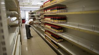 Image: A woman looks at products surrounded by empty shelves at a supermark