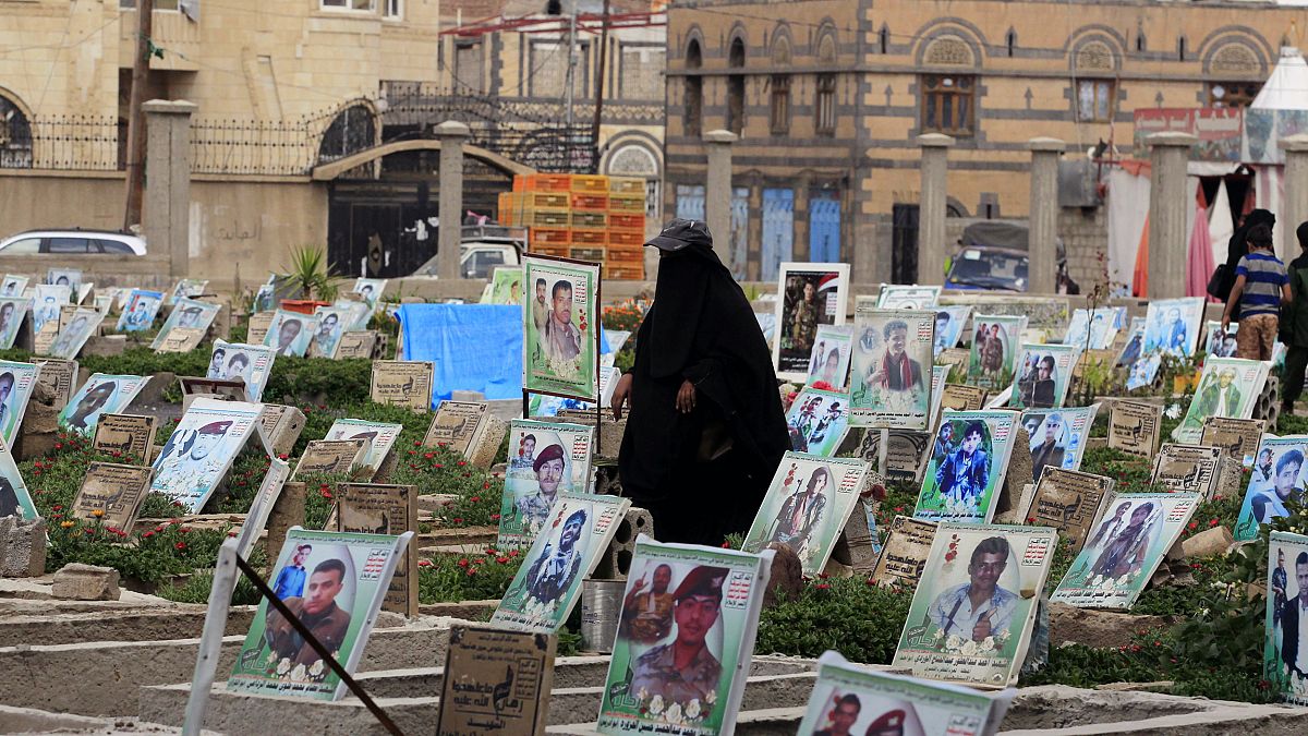 Image: A woman walks among graves with portraits of Houthi militia members
