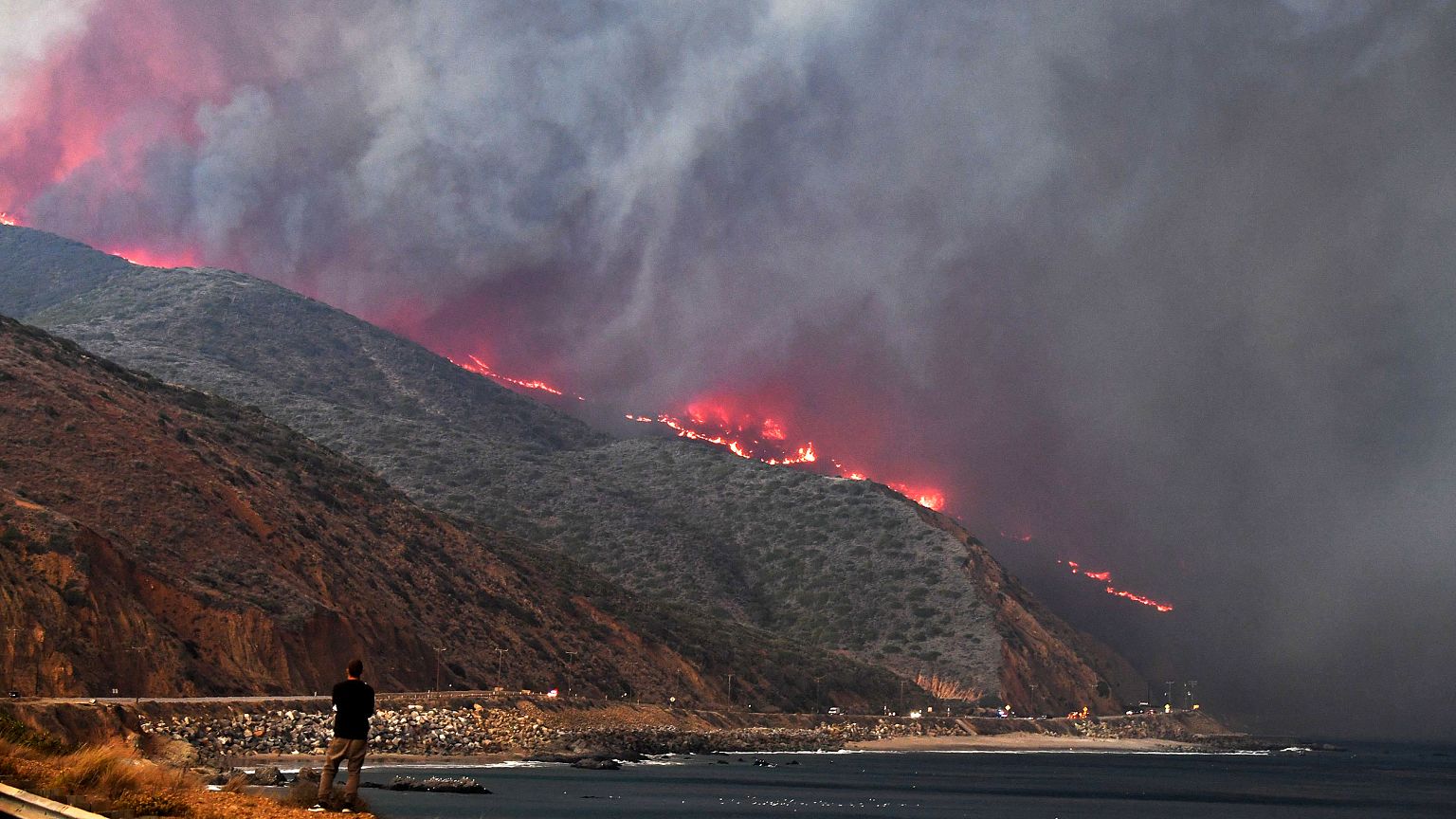 Image: A man watches as the Woolsey Fire reaches the ocean along Pacific Co