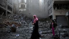 Image: A Palestinian family walks next to a destroyed residential building 