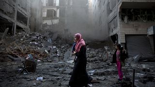 Image: A Palestinian family walks next to a destroyed residential building