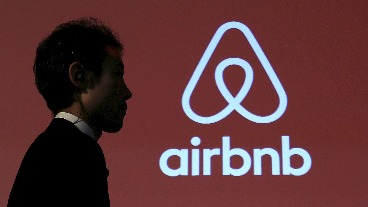 Image: A man walks past a logo of Airbnb after a news conference in Tokyo