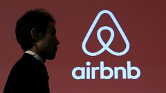 Image: A man walks past a logo of Airbnb after a news conference in Tokyo