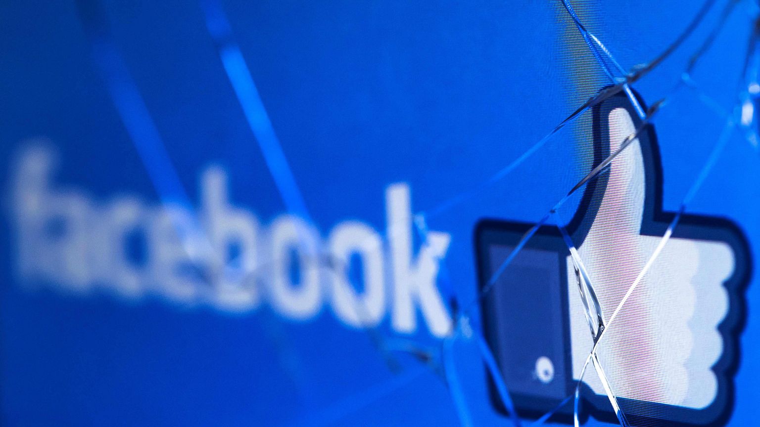 The Facebook logo on a broken screen of a mobile phone.