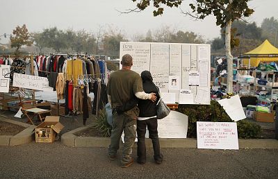 Tera Hickerson, right, and Columbus Holt embrace as they look at a board with information for services at a makeshift encampment outside a Walmart store for people displaced by the Camp Fire. 