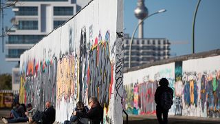 Image: People sit along the Berlin wall at the East Side Gallery in Berlin,