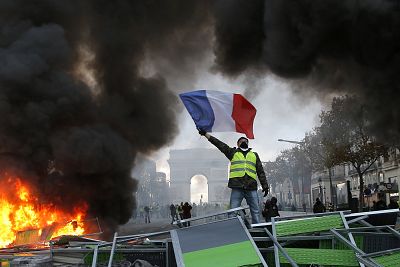 A demonstrator waves the French flag onto a burning barricade on the Champs-Elysees avenue with the Arc de Triomphe in background, during a demonstration against the rising of the fuel taxes on Nov. 24, 2018, in Paris.
