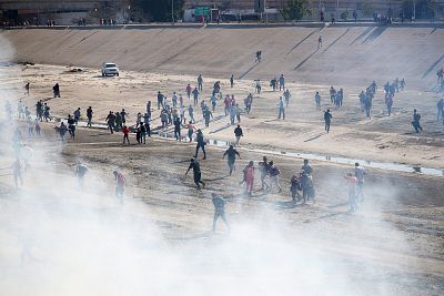 Migrants run from tear gas, thrown by the U.S border patrol, near the border fence between Mexico and the United States in Tijuana, Mexico, Nov. 25, 2018.