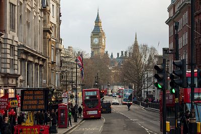 Buses pass through traffic lights near the Houses of Parliament in London.