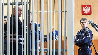 Mikhail Popkov stands inside a defendant's cage during a court hearing in I
