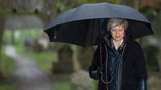 Image: Britain's Prime Minister Theresa May shelters from the rain under an