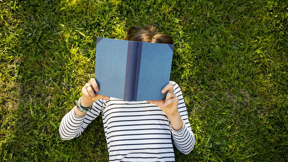 Girl lying on meadow reading a book