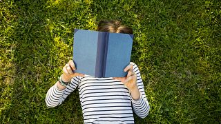 Girl lying on meadow reading a book