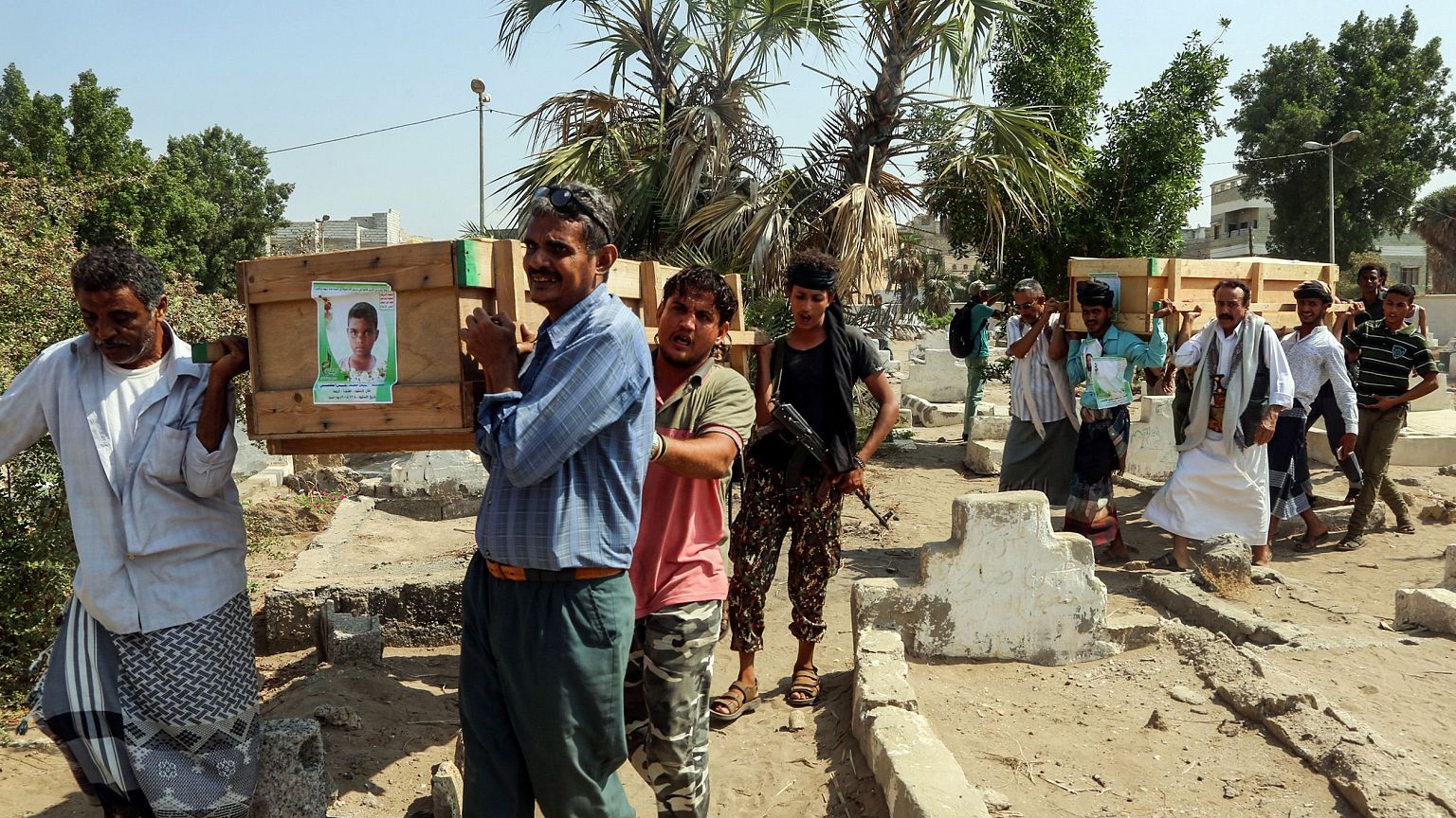 Image: Mourners walk through a cemetery carrying the coffin of one of the v