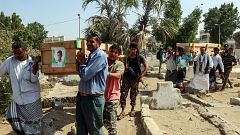 Image: Mourners walk through a cemetery carrying the coffin of one of the v