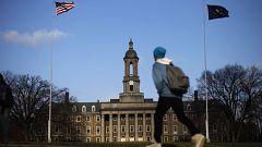 Image: A students walks in front of the Old Main building on the Penn State