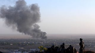 Image: Iraqi Kurdish Peshmerga fighters look on as smoke billows in the tow