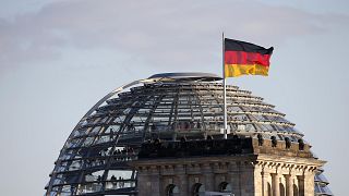 A German flag flutters next to the dome of the Reichstag building in Berlin