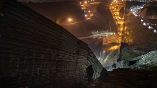 Image: Migrants looks for a place to jump over the border fence to enter th