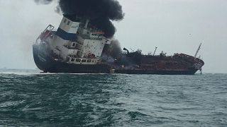 Image: Smoke rising from an oil tanker as it tilts to one side in the water