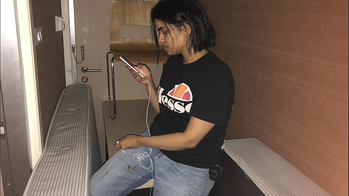 Image: Rahaf Mohammed Alqunun views her mobile phone as she sits barricaded