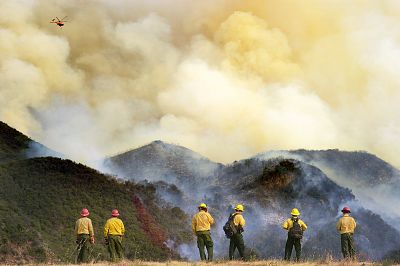 U.S. Forest Service members watch a firefighting helicopter fly over remote terrain during the 2017 Whittier Fire in Santa Barbara County.