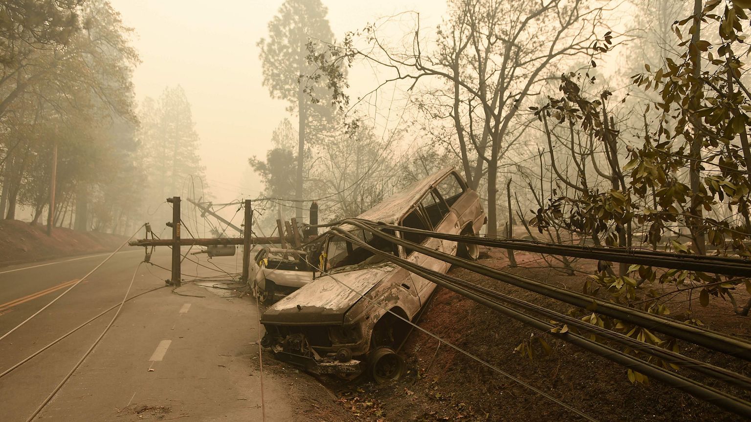 Image:  fallen power line is seen on top of burnt out vehicles on the side 