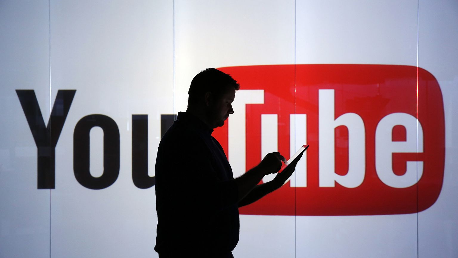 Image: A man stands in front of YouTube's logo at an office in London