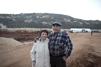 Miriam and Haim Hod stand in front a tent erected by the Israeli military over the exposed tunnel, with the border wall and the Lebanese village of Kafr Kela behind them.