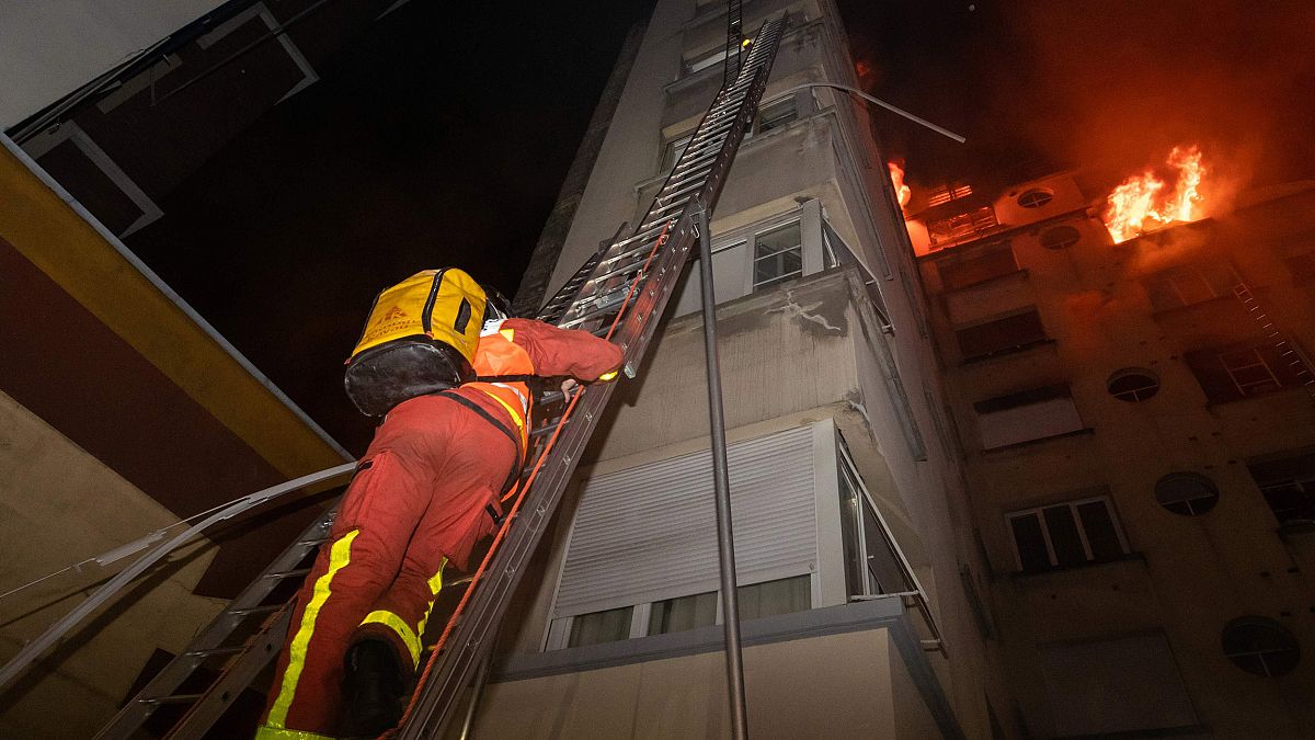 Image: A fireman climbs up a ladder to battle a fire burning in a building 