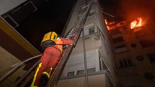 Image: A fireman climbs up a ladder to battle a fire burning in a building 